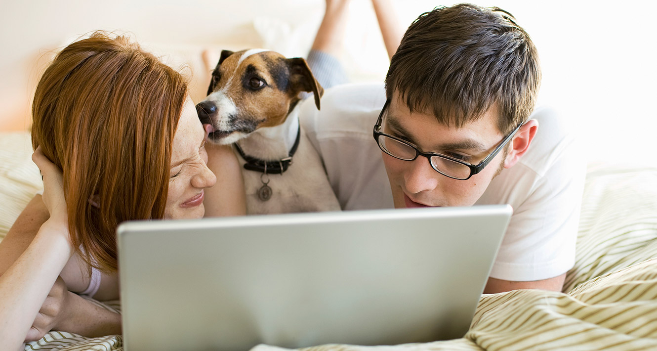 Young couple with dog using laptop on bed